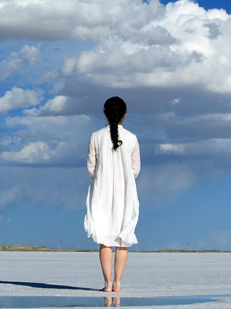 Woman stands alone on a vast salt flat under a bright blue sky with clouds.